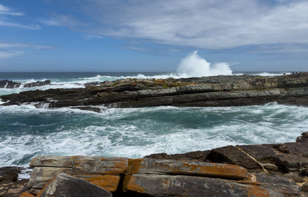 Ocean waves crashing on rocky coast, blue sky with scattered cloudsの写真素材