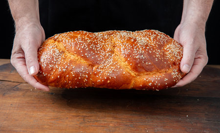 Easter sweet bread, baker hands holding a fresh baked  tsoureki braid over a wooden table, closeup...