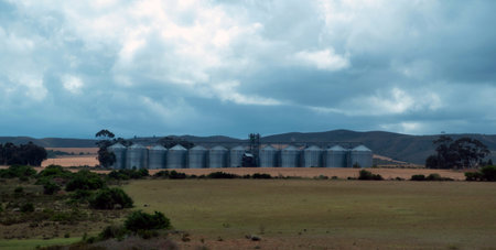 Rural agricultural landscape in South Africa. Large grain silos, rolling hills and open farmland, cloudy sky.の写真素材