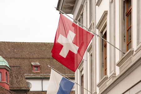Swiss flag hanging from a pole on a building facade, Traditional buildings with tiled roofs and blue and white Lucerne flag on background,の写真素材