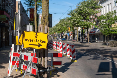 Temporary lane for pedestrians, road maintenance works in Rotterdam city. Yellow detour sign with dutch text, crossing in englishの写真素材