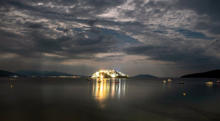 illuminated daskaleio rocky island featuring the church of the twelve apostles at night in tolo bay...