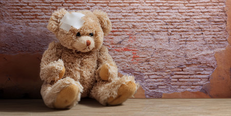 Teddy bear with white bandage on head sitting alone on wooden parquet floor. Kids injury and accident conceptの写真素材