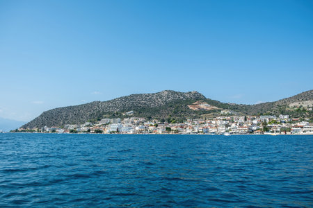 Coastal view of Tolo Greece seen from the sea. Green hills, rocky shoreline, and seaside town. Calm blue water and clear summer sky,の写真素材