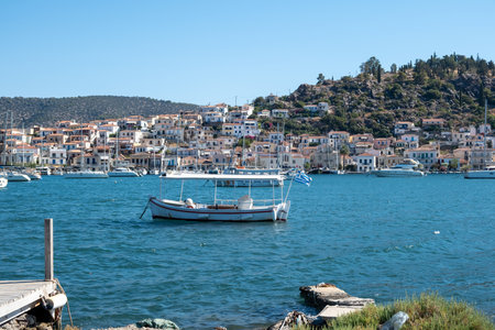 Poros Island, Greece. Fishing boat anchored on blue sea, Traditional architecture coastal town and hillside houses backgroundの写真素材