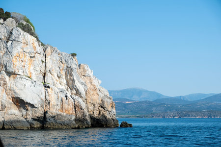 A rugged rocky coastal cliff rises above the calm blue sea, near Tolo, blue skyの写真素材