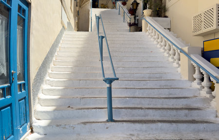 Whitewashed stone staircase with blue railings leading between traditional houses in Poros town, Greece, blue summer sky.の写真素材