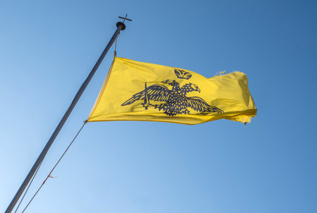 Byzantine empire and Greek Orthodox Church flag waving on blue sky. Double headed eagle on yellow