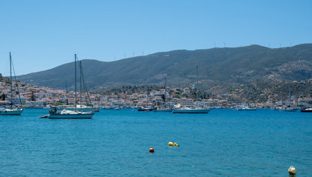 Poros Island harbor Greece. Boats floating on calm blue water, traditional architecture hillside houses, wooden pier and summer skyの写真素材
