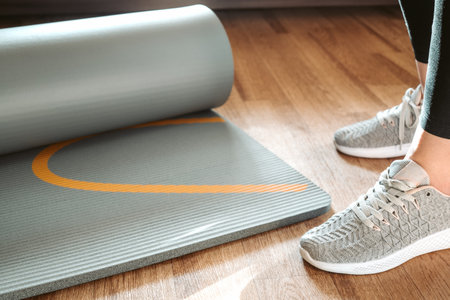 Woman stands near yoga mat rolled out on the floor ready for home fitness class, sport, acttive...