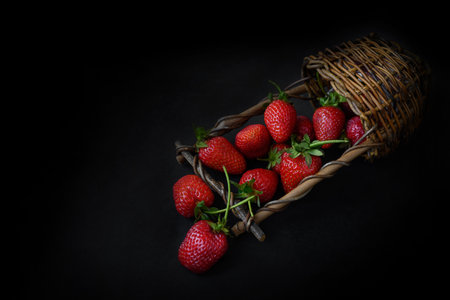 Wicker basket lays on dark surface full of red ripe srtawberries, summer food backgroundの写真素材