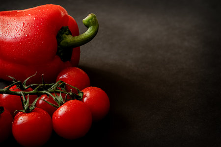 Red ripe fresh cherry tomatoes on branch and pepper on dark background. Healthy food and dietingの写真素材
