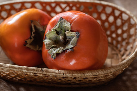 Two ripe persimmon fruit in wicker basketの写真素材