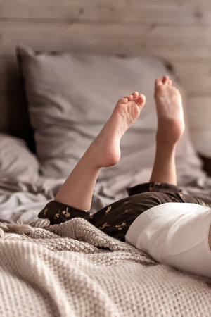 legs of kid laying on the bed in the morningの写真素材