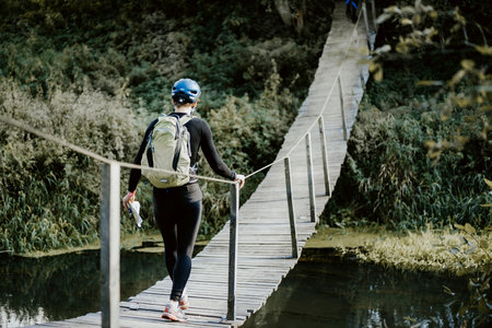 Tourist with backpack crosses the river on wooden suspension bridge