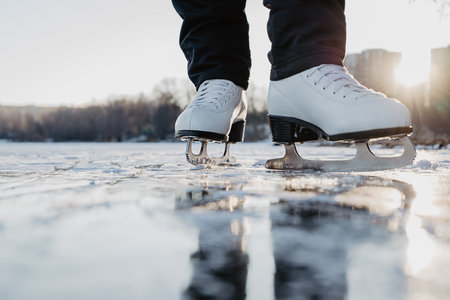 Woman wearing white figure skates stands on ice. Winter outdoor sport activities