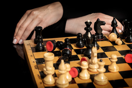 Woman ponders next move in chess game sitting in front of old wooden chessboard with randomly placed piecesの写真素材