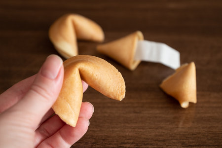 Person holding in hand fortune cookie against few cookies laying on table surface backgroundの写真素材
