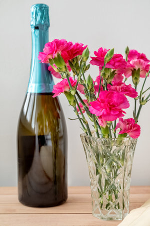 bottle of champagne and bunch of carnation flowers on the table festive decorationの写真素材