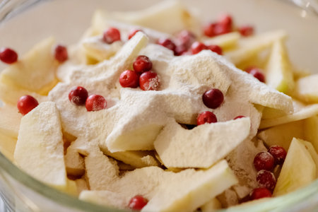 Sliced apples and cranberries sprinkled with flour in a glass bowl. Ingredients for Apple pie. Cooking at home. Homemade cakeの写真素材