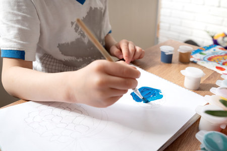 Kid drawing with blue gouache paint in album close upの写真素材