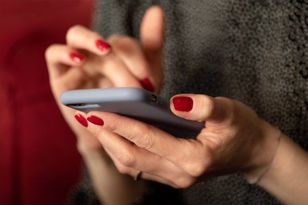 woman hands with red manicure holding mobile phone and textingの写真素材