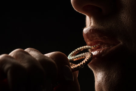 women's lips bite gold jewelry, close up, dark background