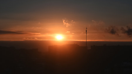 Orange sunset over roofs of multi-storey buildings on horizon, urban backgroundの写真素材