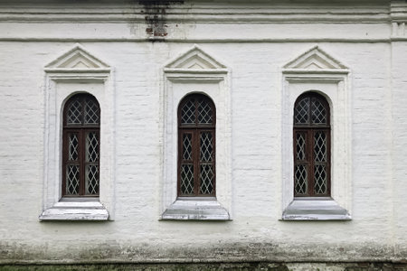 Group of three old-fashioned windows on facade of ancient white painted brick house