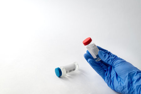 Hand in blue latex medical glove hold one ampule with vaccine with second ampoule is in the...