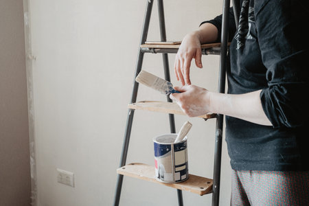 Person standing near stepladder holding paintbrush in hand. Home renovation conceptの写真素材