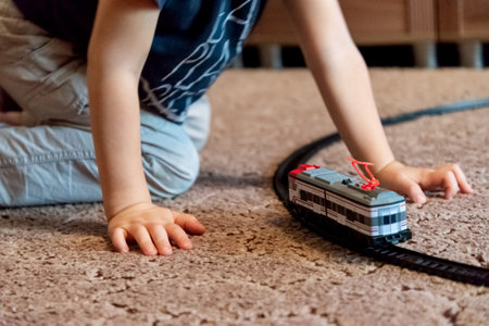 Little boy plays with toy railway  train in the room on the floor carpet