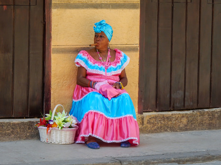 A typical cuban woman with a traditional dress smoking a cigar in a public street (05.15.2016, Havana, Cuba).のeditorial素材