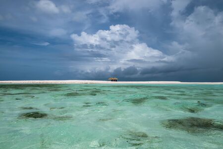 View of a little sandbank in the caribbean sea during a thunderstorm with isolated beach umbrellas and a dark background (Cayo Muerto, Los Roques Archipelago, Venezuela).の写真素材