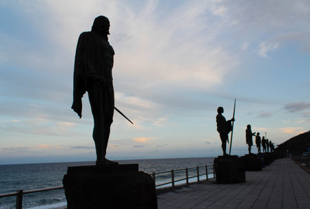 Silhouette of metal statues of Guanches kings in Candelaria,Tenerife, Canary Islands. Sunset by the sea with cloudy sky.のeditorial素材