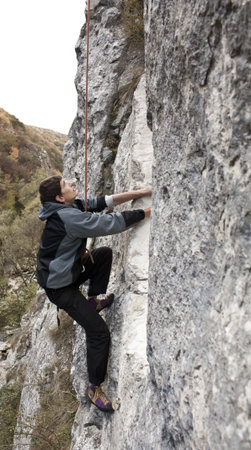 Young white man climbing a steep wall in mountainの写真素材