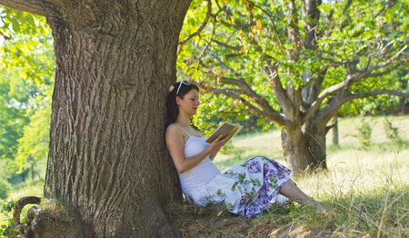Pregnant attractive woman reading in parkの写真素材