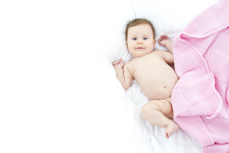 adorable baby lying in a white bed with a pink blanketの写真素材