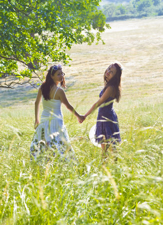 happy girls in a green field holding each other's handの写真素材