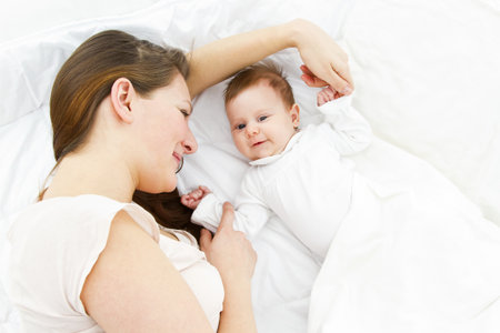 young mother lying with her baby in a white bedの写真素材