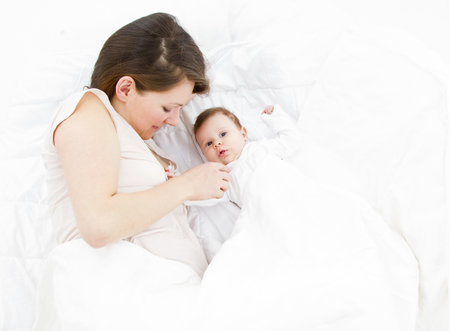 young mother lying with her baby in a white bedの写真素材