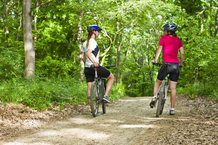 two girls riding the bicycle in the forestの写真素材