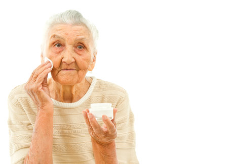 very old lady isolated on white is wiping off her face with a makeup padの写真素材