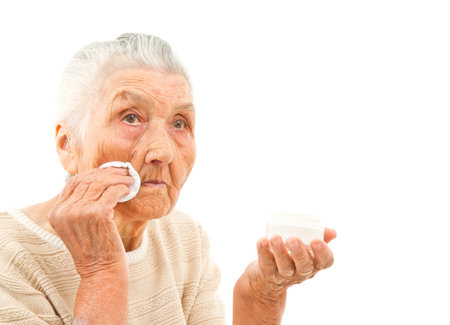 very old lady isolated on white is wiping off her face with a makeup padの写真素材