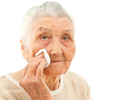 very old lady isolated on white is wiping off her face with a makeup padの写真素材