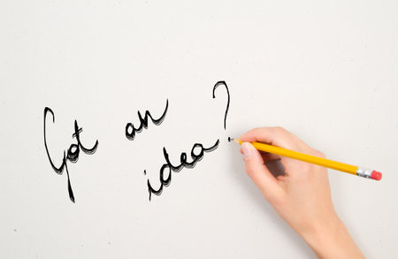 a woman's hand is writing a question  with a pencil on a white sheet of paperの写真素材