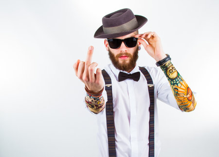 young hipster man wearing  hat , suspenders,   a bow-tie and   a funny tattoo-sleeve showing his f-fingerの写真素材