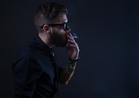 studio portrait of a hipster man smoking with black backgroundの写真素材