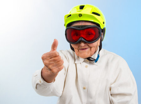 funny grandma wearing a yellow bicycle helmet and ski  goggles and showing thumbs upの写真素材