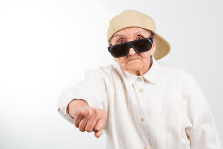 Funny grandma's studio portrait  wearing eyeglasses and baseball cap who kicks with  her fist , isolated on whiteの写真素材